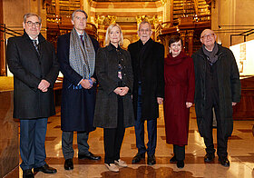 Sechs Personen in eleganter Kleidung posieren im Marmorsaal.