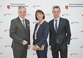 Drei Personen posieren vor Logowand.