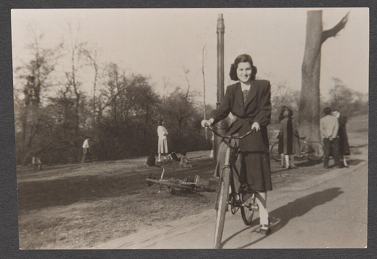 Schwarz-weißes Foto von lächelnder Frau auf einem Fahrrad in einem Park.