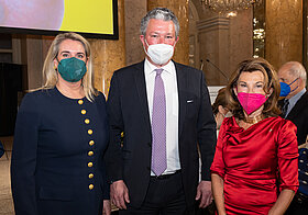 Drei Personen in eleganter Kleidung im Marmorsaal. 