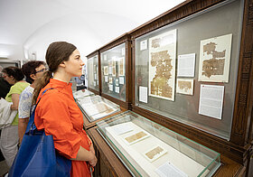 Person in orangem Kleid sieht sich eine Vitrine im Papyrusmuseum an.
