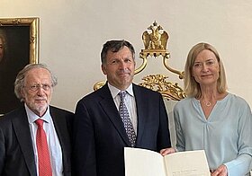 Drei Personen posieren mit Urkunde.
