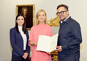 Drei Personen posieren mit einer Urkunde.