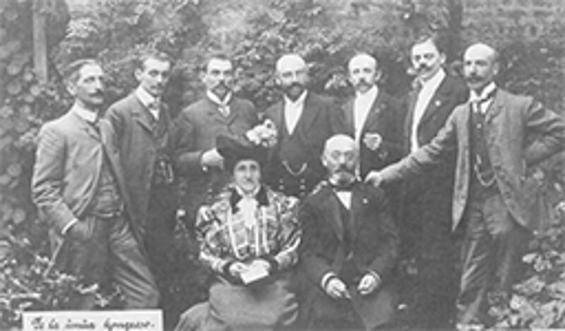 Acht elegant gekleidete Männer und eine Frau posieren draußen für ein Foto, schwarz-weiß