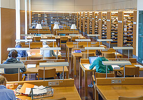 Mehrere Personen sitzen in einem Bibliothekssaal und lesen