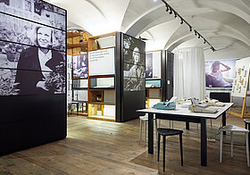 Museumsraum mit Regalen mit Fotografien, rechts ein Tisch mit Schreibmaschinen.