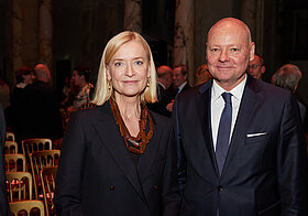 Zwei Personen in eleganter Kleidung. Ausstellungspublikum im Hintergrund zu sehen.