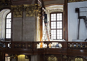 Person auf der Leiter putzt die Holzwand.