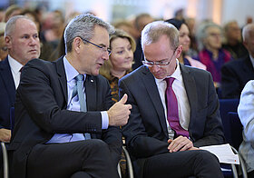 Zwei Personen sitzen in Publikum und unterhalten sich lachend.