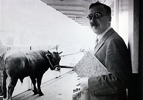 Person mit Sonnenbrille, Mappe und Zigarette rechts, links Stier.
