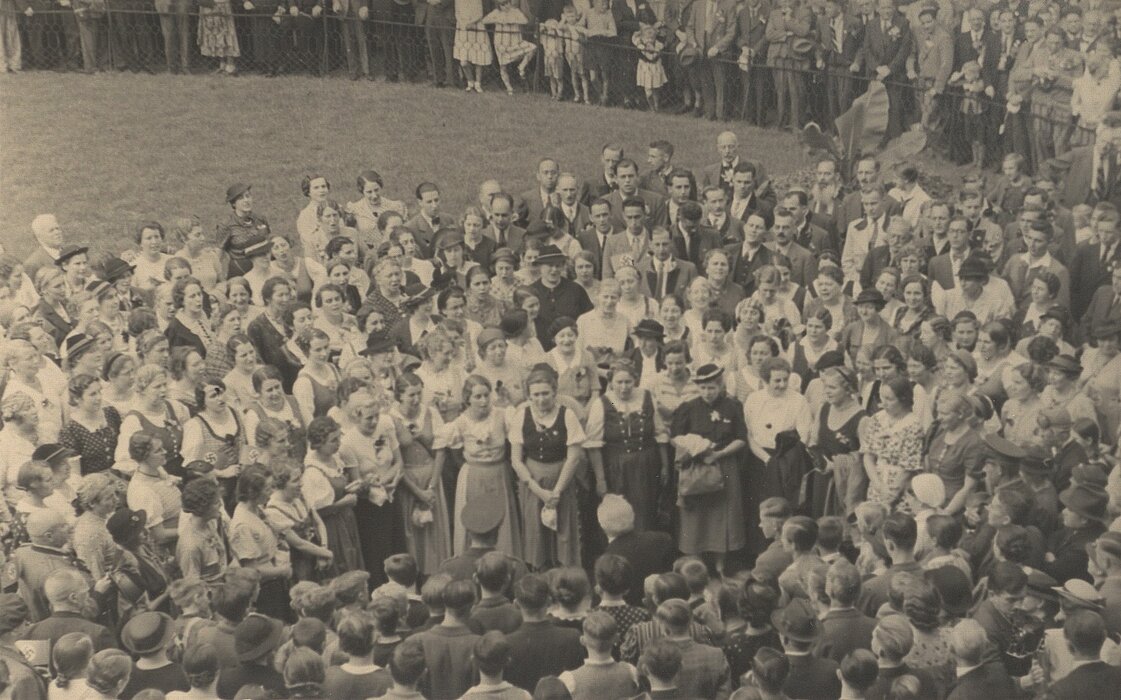 Menschenmenge in Tracht auf Wiese.
