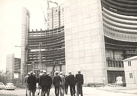 Schwarz-Weiß-Foto von mehreren Menschen vor einem im Bau befindlichen Gebäude.