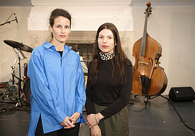 Zwei Personen stehen vor einer Bühne mit Musikinstrumenten und posieren für ein Foto. 