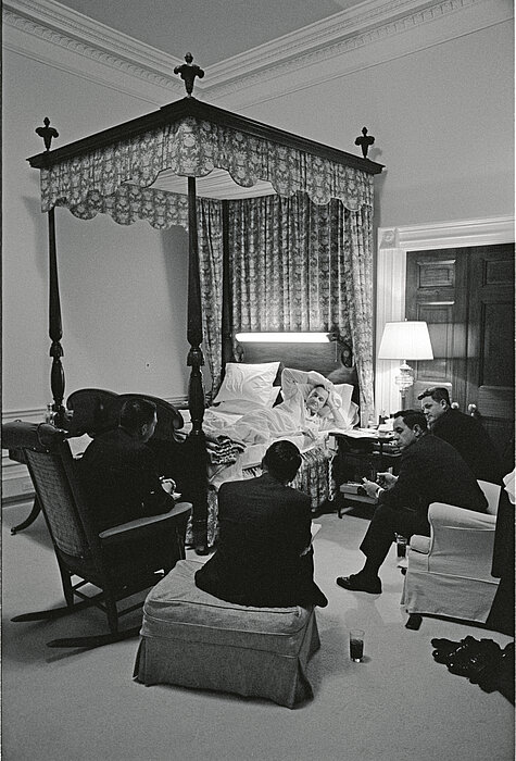 Schwarz-weißes Foto von Personen die in Schlafzimmer sitzen.
