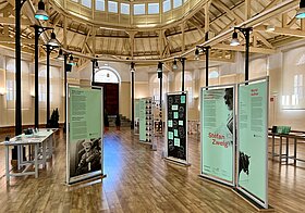 Schöner Ausstellungssaal, schwarze Scheinwerferstelen, Dachschrägen-Gebälk, darüber Fenster