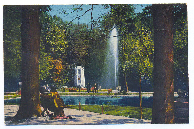 Bunte Postkarte mit weißem Denkmal neben Teich mit Fontäne.