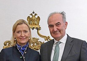 Zwei Personen in eleganter Kleidung halten ein Dokument.