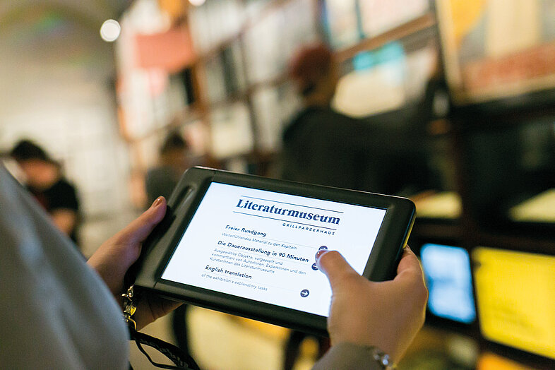 Foto von Tablet, das von Person in der Hand gehalten wird, darauf zu sehen ist ein Text über das Literaturmuseum.
