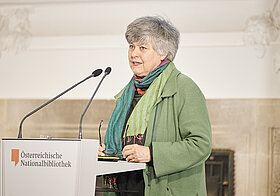 Person mit grünem Oberteil am Rednerpult.