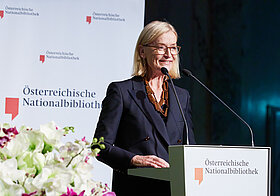 Person lächelnd am Rednerpult. 