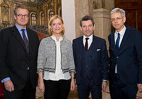 Vier Personen in eleganter Kleidung stehen nebeneinander posieren lächelnd.