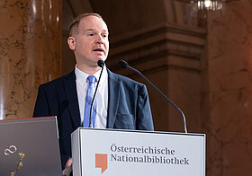 Person im Anzug steht an einem Rednerpult.