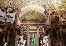 Prunkvoller Saal mit grün beleuchteter Statue in der Mitte.