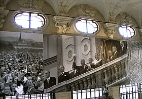 Fotos von Menschenmenge und Personen, die lachend den Staatsvertrag halten, in einem alten Gebäude aufgehängt.