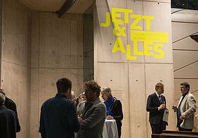 Menschen bei Ausstellung, an der Wand ein greller Schriftzug.