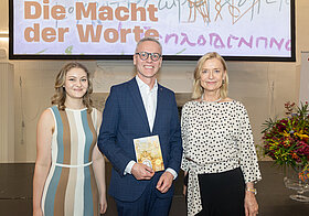 Drei Personen posieren vor Bühne.
