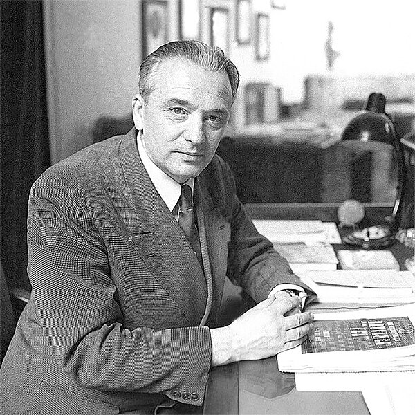 Schwarz-weißes Foto von einem Mann im Anzug, der an einem Schreibtisch sitzt