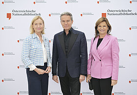 Drei Personen posieren vor einer Logowand.