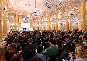 Volles Publikum in einem Marmorsaal von hinten fotografiert.