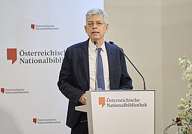 Mann steht vor einem Podium und hält eine Rede. 