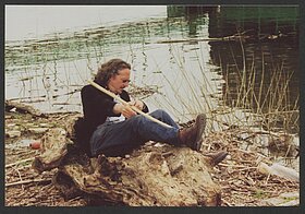 Foto von Person, die neben Fluss auf einem Baumstamm liegt.