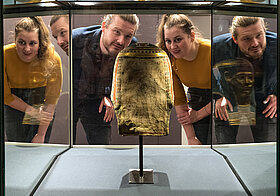 Zwei Personen betrachten einen goldenen Pharaonenkopf in einer Vitrine