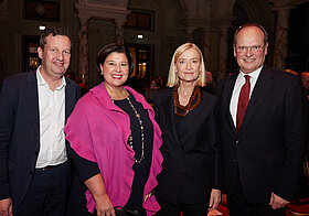 Foto von vier Personen, die lächelnd posieren. 