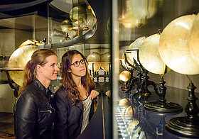Zwei Personen betrachten Globen in einer Vitrine
