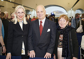 Drei elegant gekleidete Personen posieren lächelnd.