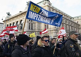 Demonstrierende mit rot-weißen-roten Flaggen und Transparent mit Text "Nein zum Impfzwang".