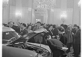 Menschen begutachten ein Auto auf einer Messe in einem prunkvollem Saal
