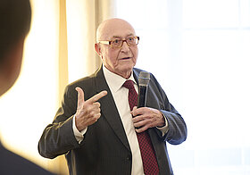 Person in Anzug hält eine Rede mit Mikro.