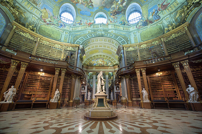 Hoher Saal unter einer barocken Kuppeldecke mit Statuen und Bücherregalen