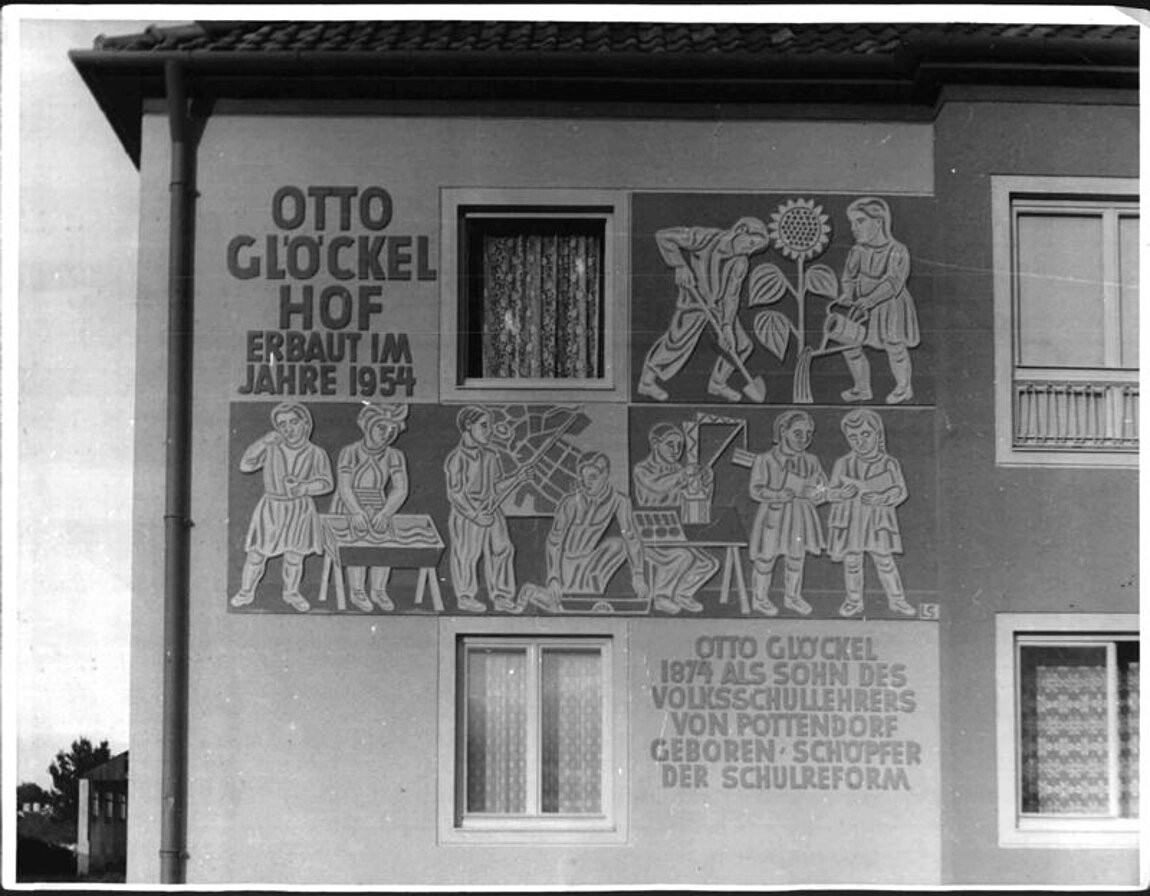 Schwar-weißes Foto von Hausfront mit Gemälde, das Menschen beim Handwerk zeigt.