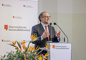 Person spricht in Mikro auf Bühne.
