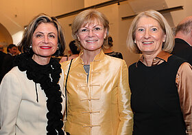 Drei blonde Personen in eleganter Kleidung posieren lächelnd. 