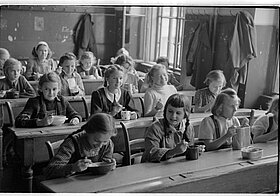 Kinder sitzen in Schulbänken und essen