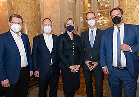 Fünf Personen in Anzügen stehen im Marmorsaal und posieren zur Kamera.