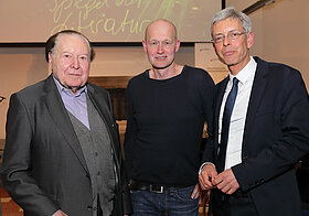 Drei Personen posieren nebeneinander vor einer Leinwand.