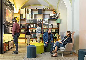 Personen in einem Museum mit alten Bücherregalen und Sitzmöglichkeiten